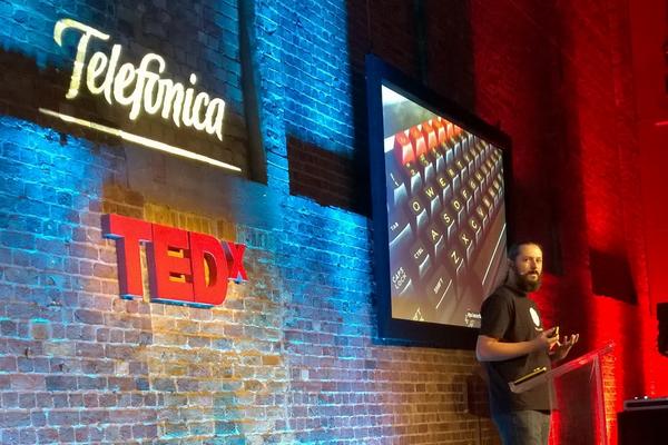 Terence Eden standing in front of the TEDx logo. A projection screen shows the keyboard of an old fashioned BBC Micro computer
