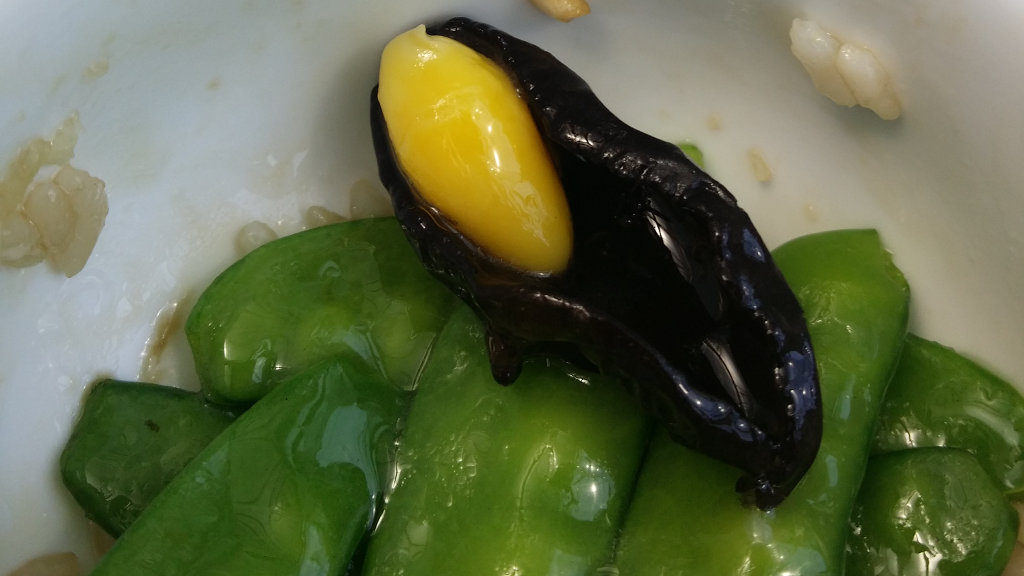 A mysterious yellow vegetable nestles inside a mushroom. Green beans surround it.